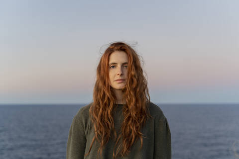 Porträt einer rothaarigen jungen Frau an der Küste bei Sonnenuntergang, Ibiza, Spanien, lizenzfreies Stockfoto
