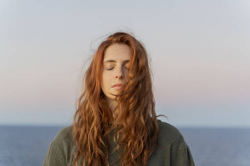 Redheaded young woman with closed eyes at the coast at sunset, Ibiza, Spain - AFVF04872