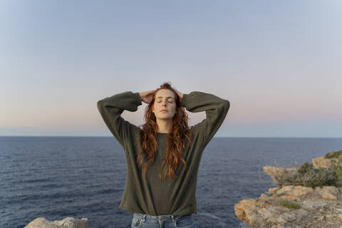 Rothaarige junge Frau an der Küste bei Sonnenuntergang, Ibiza, Spanien, lizenzfreies Stockfoto