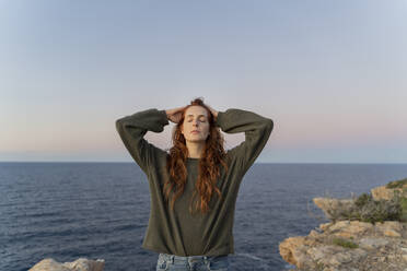 Rothaarige junge Frau an der Küste bei Sonnenuntergang, Ibiza, Spanien - AFVF04873