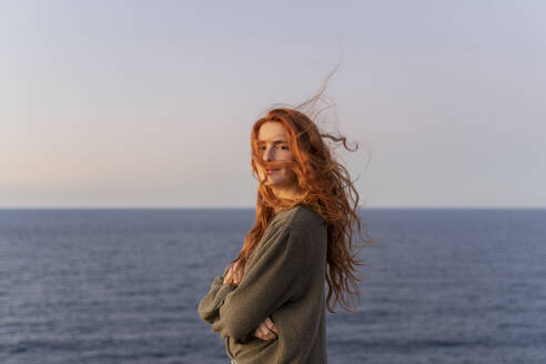 Portrait of redheaded young woman with windswept hair at the coast at sunset, Ibiza, Spain - AFVF04874