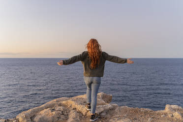 Redheaded young woman standing at the coast at sunset, Ibiza, Spain - AFVF04875