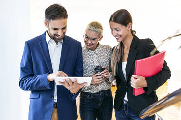 Businessman showing tablet to smiling colleagues in office - JSRF00734