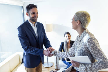 Businesswoman and businessman shaking hands in lounge - JSRF00752