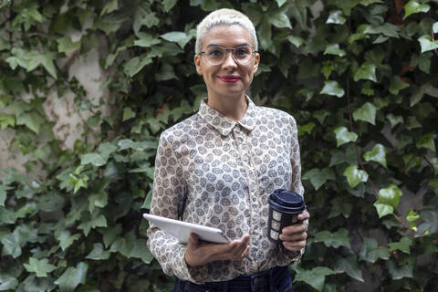 Portrait of confident businesswoman with takeaway coffee and tablet outdoors stock photo