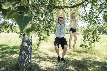Portrait of smiling father and daughter hanging on a branch of a birch tree - WFF00239