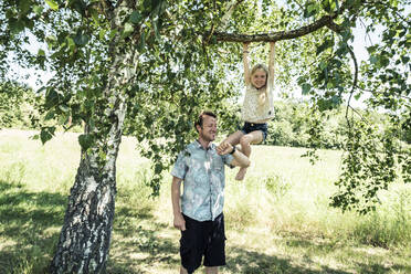 Father checking the time with daughter hanging on a branch of a birch tree - WFF00243