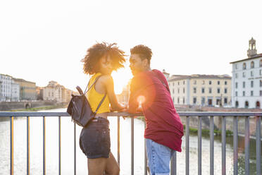 Junges Touristenpaar auf einer Brücke über dem Fluss Arno bei Sonnenuntergang, Florenz, Italien - FBAF01157