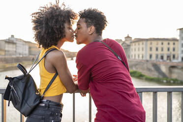 Junges Touristenpaar küsst sich auf einer Brücke über dem Fluss Arno bei Sonnenuntergang, Florenz, Italien - FBAF01158