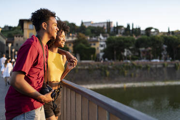 Glückliches junges Touristenpaar auf einer Brücke über den Fluss Arno bei Sonnenuntergang, Florenz, Italien - FBAF01166