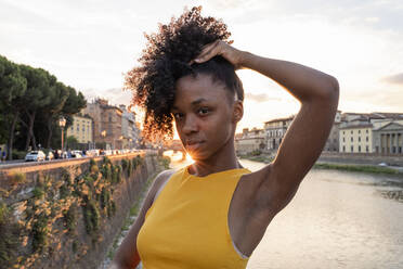Porträt einer selbstbewussten jungen Frau am Fluss Arno bei Sonnenuntergang, Florenz, Italien - FBAF01172