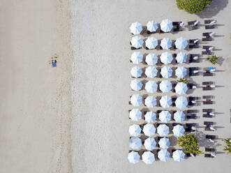 Indonesien, Bali, Luftaufnahme eines Mannes beim Sonnenbaden vor einer Reihe von Sonnenschirmen am Sandstrand von Nusa Dua - KNTF04033