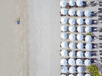 Indonesien, Bali, Luftaufnahme eines Mannes beim Sonnenbaden vor einer Reihe von Sonnenschirmen am Sandstrand von Nusa Dua - KNTF04034