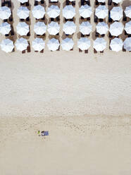 Indonesien, Bali, Luftaufnahme eines Mannes beim Sonnenbaden vor einer Reihe von Sonnenschirmen am Sandstrand von Nusa Dua - KNTF04036