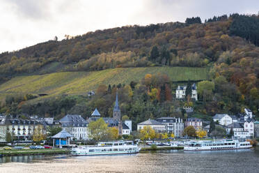 Deutschland, Rheinland-Pfalz, Traben-Trarbach, Fähren vor den Häusern der Stadt am Fluss mit einem Weinberg im Hintergrund - FCF01864