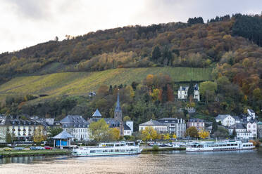 Germany, Rhineland-Palatinate, Traben-Trarbach, Ferries moored in front of houses of riverside town with hillside vineyard in background - FCF01864