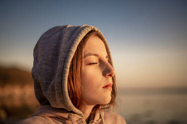 Deutschland, Mecklenburg-Vorpommern, Insel Poel, Nahaufnahme eines jungen Mädchens mit geschlossenen Augen am Strand bei Sonnenuntergang - BFRF02167