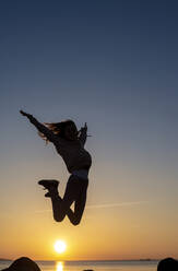 Germany, Mecklenburg-West Pomerania, Poel Island, Silhouette of teenage girl jumping by sea at sunset - BFRF02169