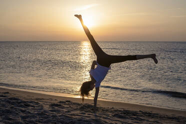 Deutschland, Mecklenburg-Vorpommern, Silhouette eines jungen Mädchens, das bei Sonnenuntergang am Strand einen Handstand macht - BFRF02174