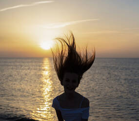 Germany, Mecklenburg-West Pomerania, Silhouette of teenage girl tossing hair on beach at sunset - BFRF02175