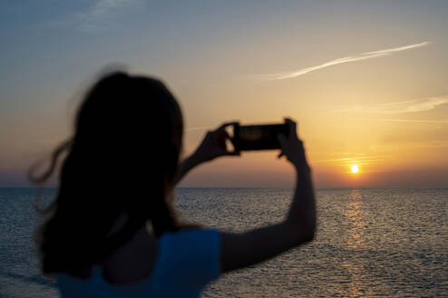 Deutschland, Mecklenburg-Vorpommern, Rückansicht eines jugendlichen Mädchens beim Fotografieren des Meeres bei Sonnenuntergang - BFRF02176