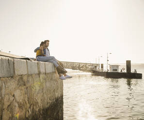 Junges Paar sitzt auf dem Pier am Wasser und genießt die Aussicht, Lissabon, Portugal - UUF19814