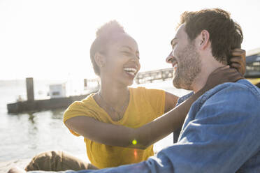 Happy young couple sitting at the waterfront, Lisbon, Portugal - UUF19824