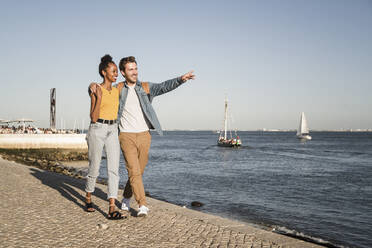 Glückliches junges Paar beim Spaziergang auf dem Pier am Wasser, Lissabon, Portugal - UUF19859