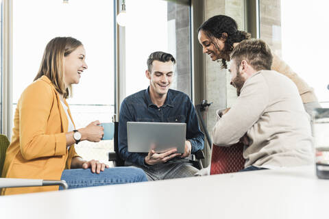 Glückliche junge Geschäftsleute mit Laptop bei einem Treffen im Büro, lizenzfreies Stockfoto