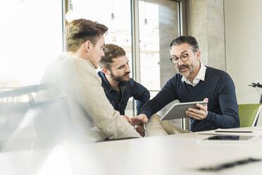 Three businessmen having a meeting in office sharing a tablet - UUF19941