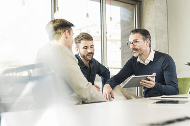 Three businessmen having a meeting in office sharing a tablet - UUF19942