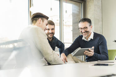 Three happy businessmen having a meeting in office sharing a tablet - UUF19943