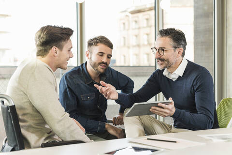 Drei Geschäftsleute bei einem Treffen im Büro, die sich ein Tablet teilen, lizenzfreies Stockfoto