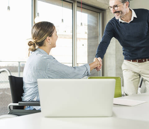 Älterer Geschäftsmann und junge Geschäftsfrau schütteln Hände am Schreibtisch im Büro, lizenzfreies Stockfoto