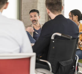 Business people having a meeting in office with one sitting in wheelchair - UUF19993