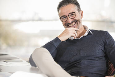 Portrait of a happy mature businessman sitting at desk in office - UUF19997