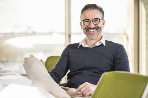 Portrait of a smiling mature businessman sitting at desk in office stock photo