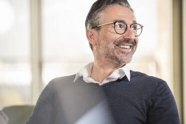 Portrait of a smiling mature businessman in office looking sideways - UUF19999