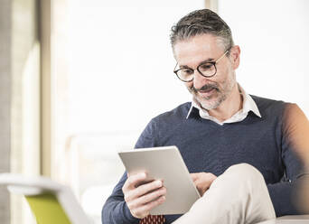 Smiling mature businessman using tablet in office - UUF20003