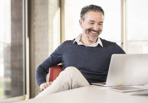 Smiling mature businessman sitting at desk in office using laptop stock photo