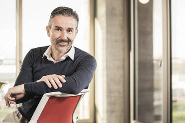 Portrait of a confident mature businessman sitting on chair in office - UUF20008