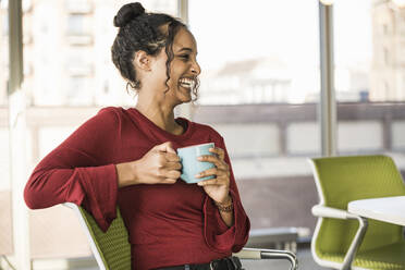 Happy young businesswoman having a coffee break in office - UUF20011