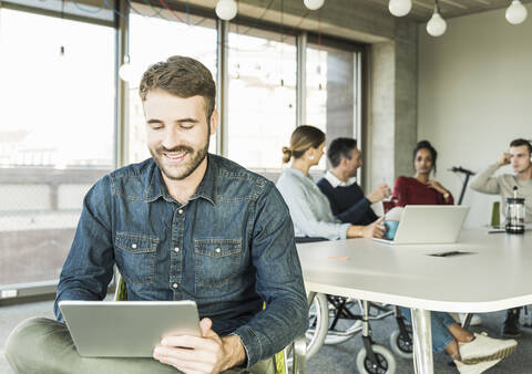 Lächelnder junger Geschäftsmann, der ein Tablet während einer Besprechung im Büro benutzt, lizenzfreies Stockfoto