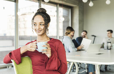 Smiling young businesswoman having a coffee break during a meeting in office - UUF20021