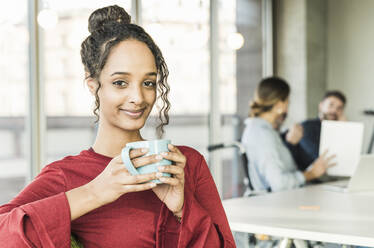 Porträt einer lächelnden jungen Geschäftsfrau in einer Kaffeepause während einer Sitzung im Büro - UUF20022