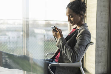 Young businesswoman using cell phone at the window in office - UUF20028