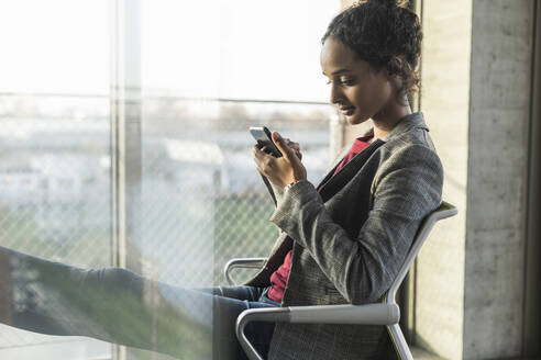 Junge Geschäftsfrau benutzt Handy am Fenster im Büro - UUF20028