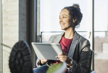 Happy young businesswoman using a tablet at the window in office - UUF20030