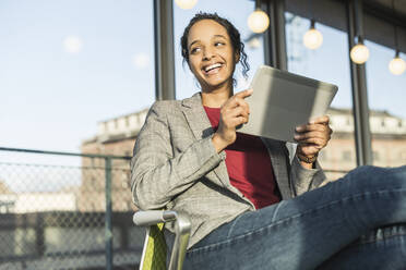 Happy young businesswoman using a tablet at the window in office - UUF20031