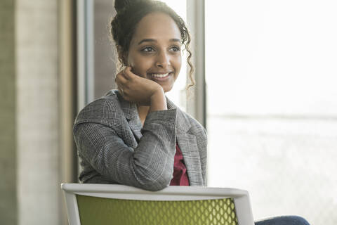 Smiling young businesswoman sitting on a chair in office stock photo